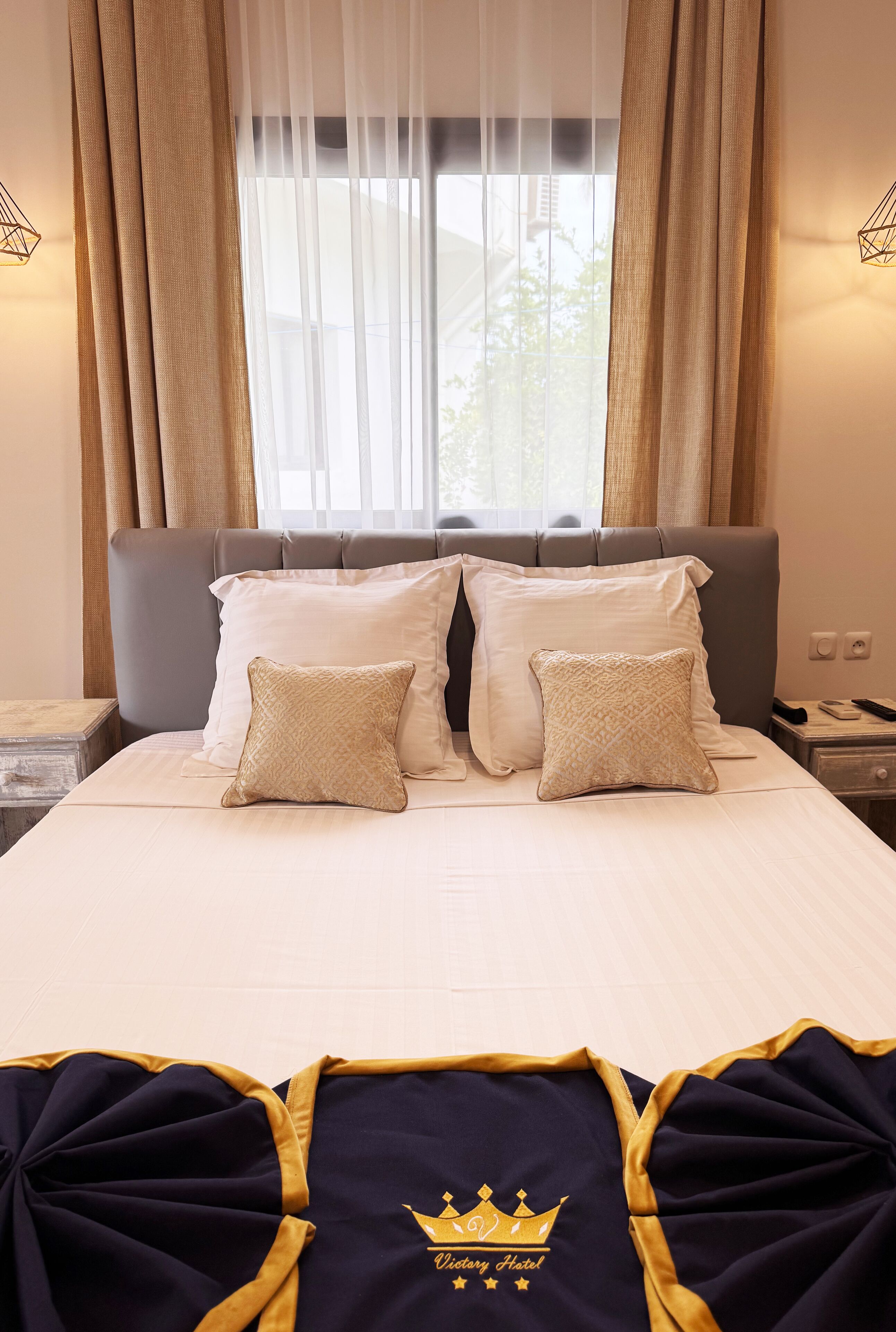 A hotel room with a bed, two pillows, a nightstand, and a window with curtains.