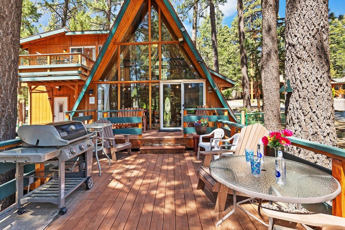 Une terrasse en bois avec des meubles d’extérieur, un barbecue et une table en verre décorée de fleurs.