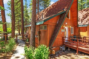 A wooden cabin with a porch, surrounded by tall trees.