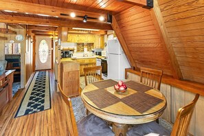 Ein gemütliches Blockhaus-Interieur mit einem Holzesstisch, Stühlen, einer Küchenzeile mit Holzschränken und einem eingebauten Kühlschrank.