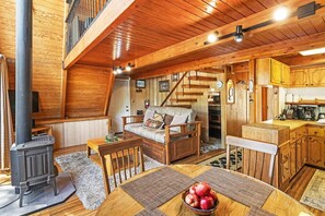 A wooden interior with a sofa, dining table, and a kitchen area. - Charming A Frame Cabin! Pet Friendly! Cozy 2 Bedroom! HOT TUB! Foosball Table! Wood Burning Fireplace! ½ Mile to Bear Mountain & Golf Course! (Big Bear Lake CA)