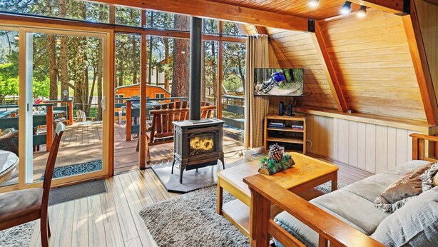 A cozy cabin interior with a large wooden ceiling, a fireplace, and a sliding glass door leading to an outdoor deck.
