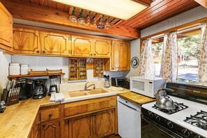 A kitchen with wooden cabinets, a stove, a microwave, and a sink. - Charming A Frame Cabin! Pet Friendly! Cozy 2 Bedroom! HOT TUB! Foosball Table! Wood Burning Fireplace! ½ Mile to Bear Mountain & Golf Course! (Big Bear Lake CA)