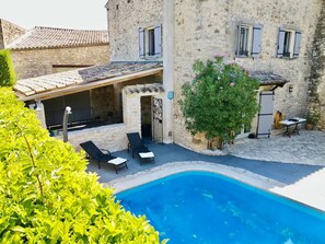Un edificio de piedra con piscina, mobiliario de exterior y un patio cubierto.
