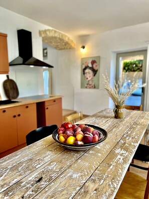 Una mesa de comedor con un frutero, armarios de madera, una campana extractora negra y un cuadro en la pared.
