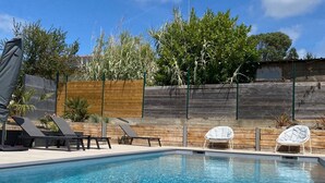 Una piscina con agua cristalina azul, rodeada de sillas de descanso y una valla de madera.