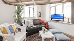 A living room with a black leather sofa, a white wicker chair, a small white table, and a TV on a stand. - Inviting 3-bed Apartment in Roma 4mins to Colosseo (Rome)