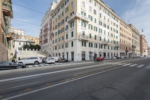 A multi-story building with a prominent entrance, a staircase leading to the ground floor, and a parking area with several cars. - Inviting 3-bed Apartment in Roma 4mins to Colosseo (Rome)