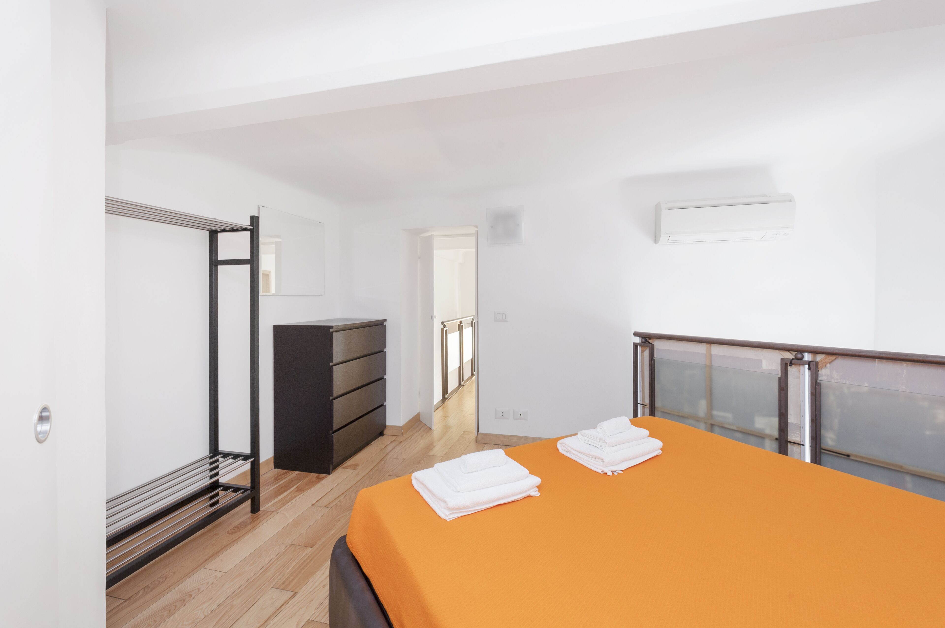 A modern hotel room with a bed, a dresser, a walk-in closet, and a balcony.