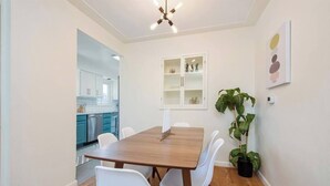 A dining area with a wooden table and white chairs, a potted plant, and a wall-mounted shelf with decorative items. - Peaceful home with fire pit and game room (Denver)