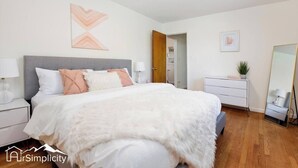 A bedroom with a large bed, bedside tables, a dresser, a mirror, and a door leading to a bathroom. - Peaceful home with fire pit and game room (Denver)