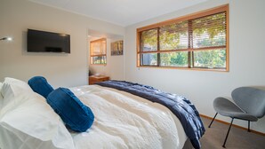 Une chambre à coucher avec un lit, une télévision, une fenêtre avec des stores et une chaise.