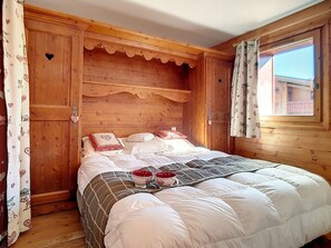 Een houten kamer met een bed, gordijnen en een raam.
