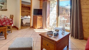 A cozy room with a wooden floor, a dining table with chairs, a TV on a wooden cabinet, and a large window with curtains. - Bright 3-room apartment with balcony, close to slopes (Les Menuires)