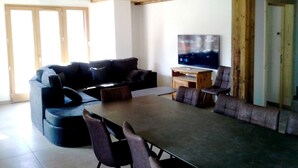 A modern living room with a sectional sofa, a dining table with chairs, a flat-screen TV on a wooden stand, and a large window providing natural light. - Duplex 5 rooms, 10 people, south, pets allowed, private parking (Valloire)