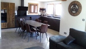 A modern kitchen with a dining area, featuring a wooden ceiling, a large round clock, and a black sofa. - Duplex 5 rooms, 10 people, south, pets allowed, private parking (Valloire)