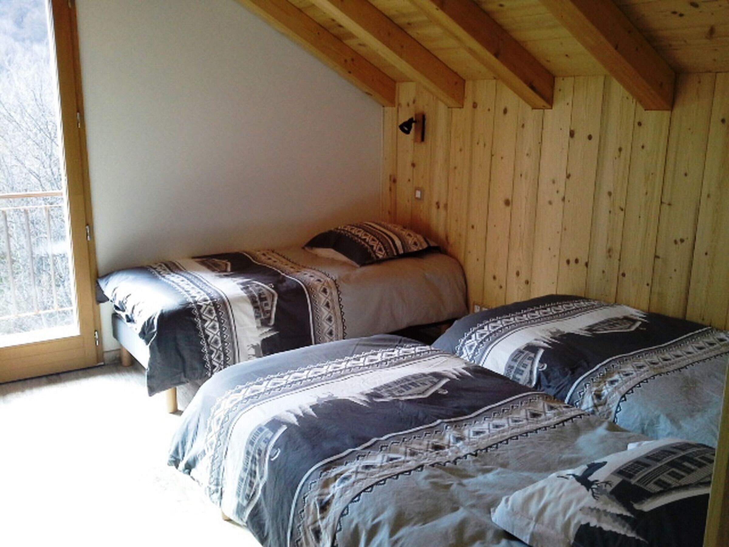 A bedroom with two beds, wooden walls, and a window.