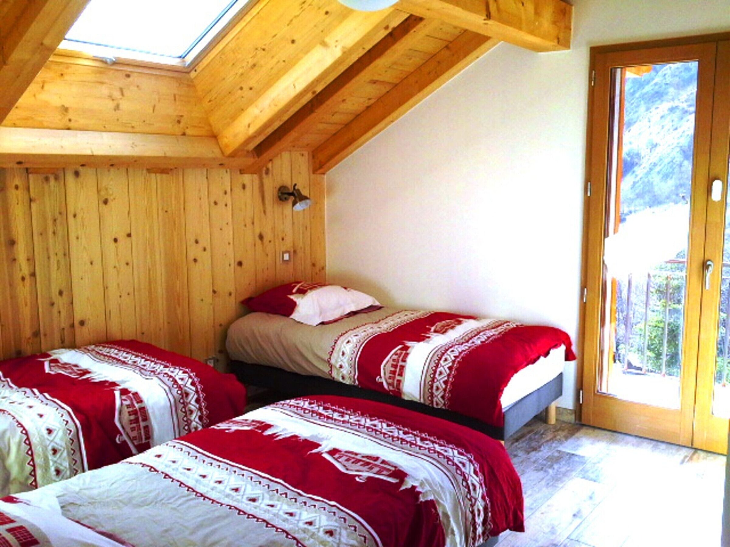 Una habitación de madera con dos camas, un tragaluz y una puerta que da a un espacio al aire libre.