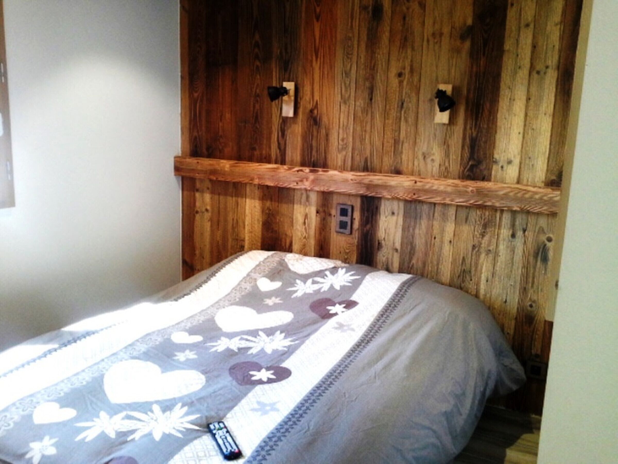 Quarto com cabeceira de madeira, cama com colcha estampada e controle remoto sobre a cama.