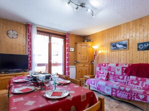 Ein gemütlicher Raum mit Holzwänden, einem Esstisch gedeckt mit Tellern und Gläsern, einem Sofa mit herzförmigem Bezug und einem Fernseher links.