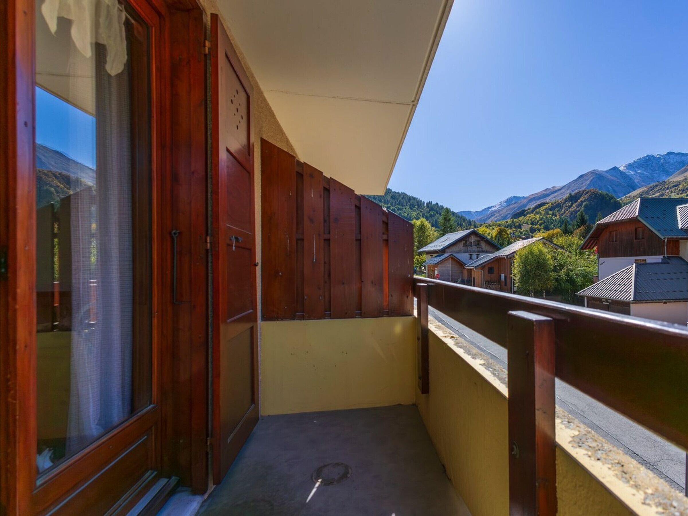 A balcony with wooden shutters, a view of a mountain landscape, and traditional buildings in the background.