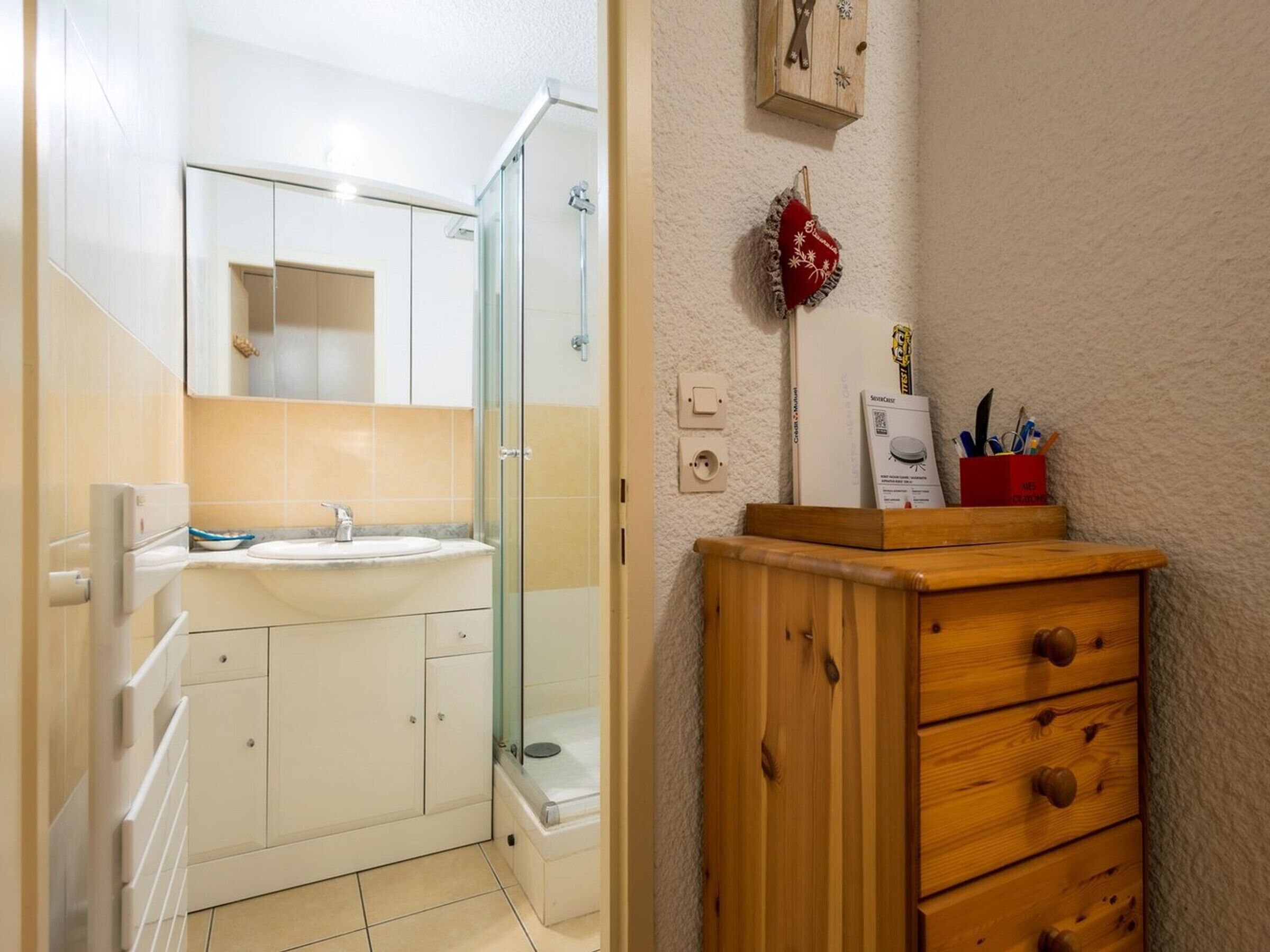 A bathroom with a glass shower enclosure, a sink, and a wooden cabinet with drawers.