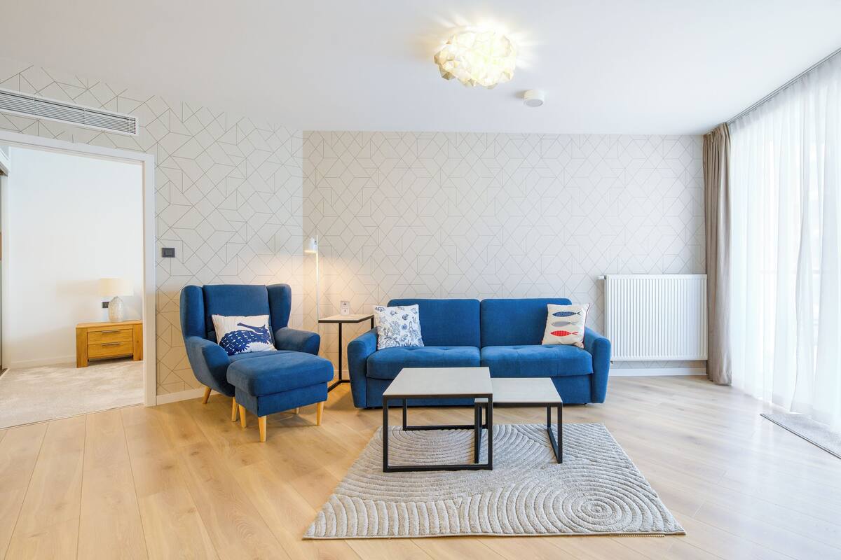 A modern living room with a blue sofa, a blue armchair, a small table, and a floor lamp.