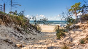 A sandy beach path leading to the ocean, surrounded by vegetation and a lifeguard tower. - Apartamenty Sun & Snow w obiekcie Pinea (Rewal)