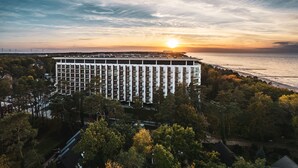 A high-rise hotel with a modern design, featuring a large number of balconies and a view of the sea at sunset. - Apartamenty Sun & Snow Qinea (Rewal)