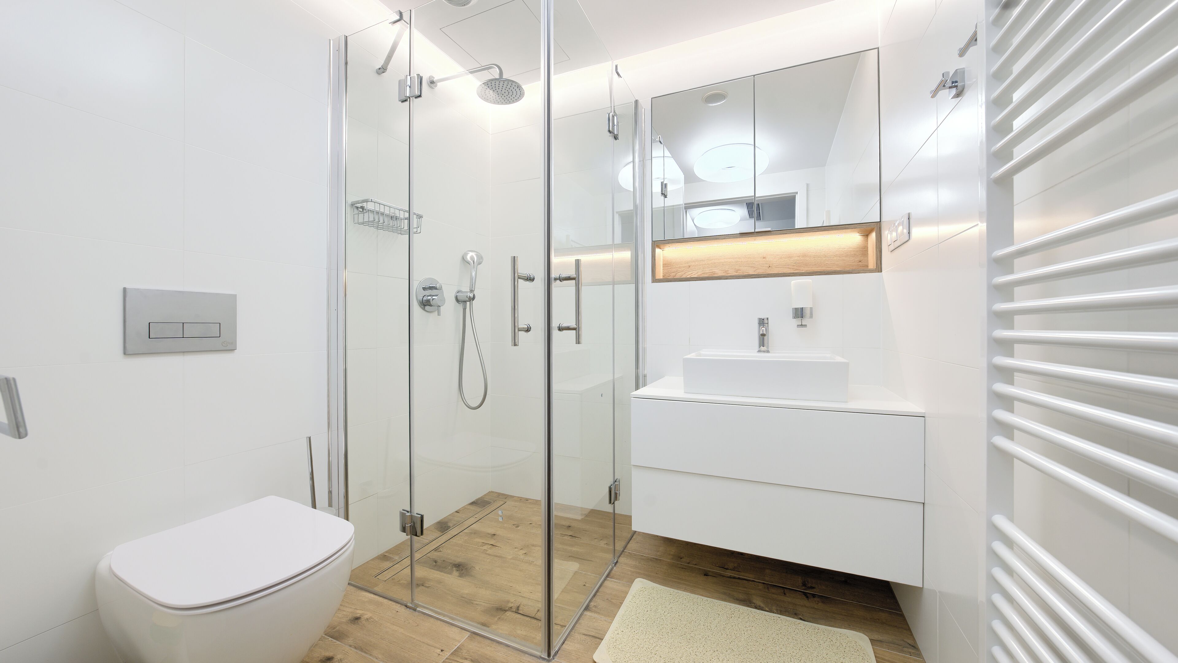 Une salle de bain moderne avec une douche à parois de verre, des toilettes blanches, un lavabo avec un miroir au-dessus et un plancher en bois.