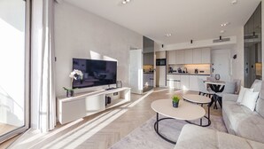 A modern living room with a flat-screen TV, a dining area with a round table, and a kitchen in the background. - Apartamenty Sun & Snow Qinea (Rewal)