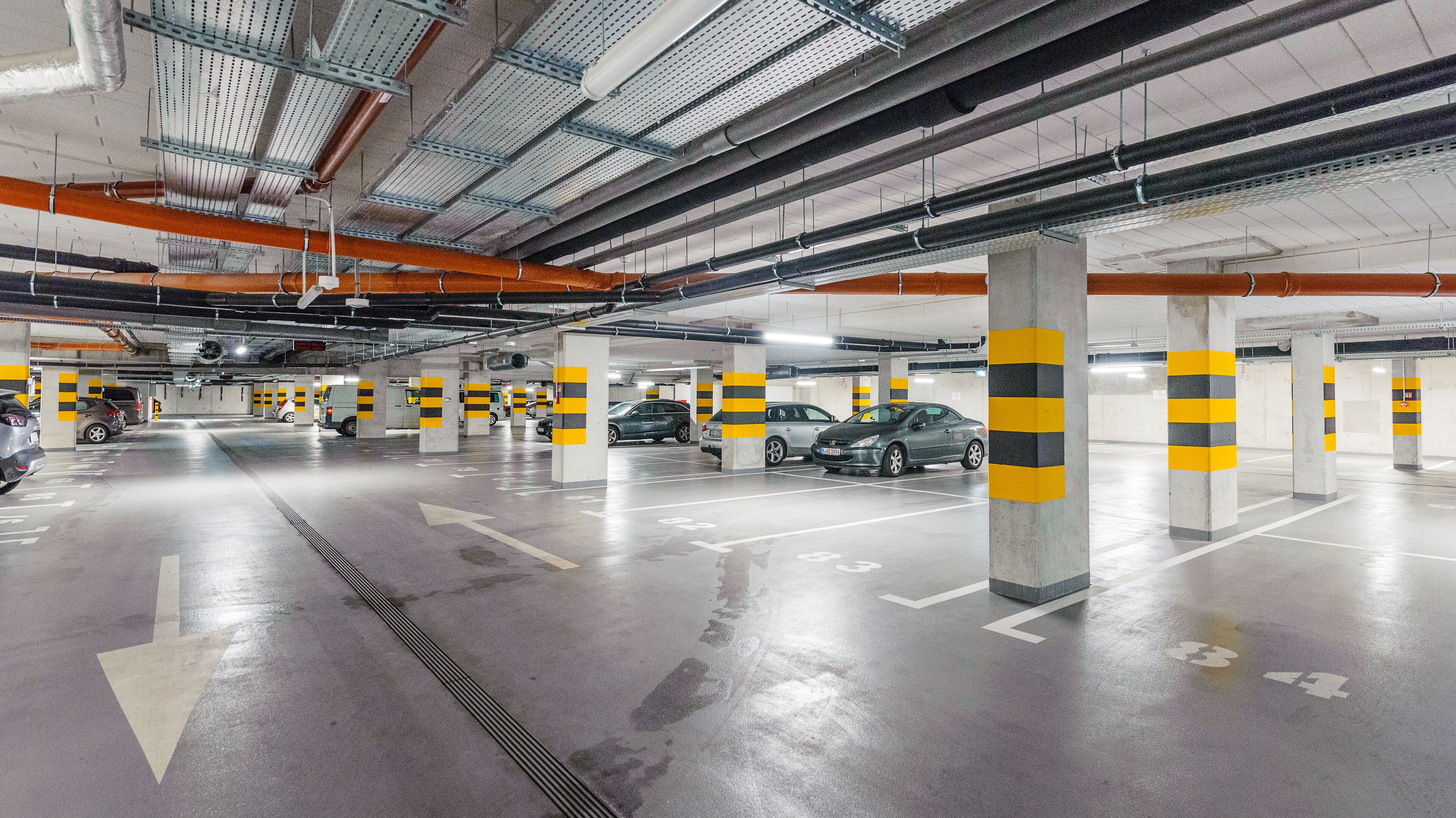 A multi-level underground parking garage with concrete pillars, clear directional arrows, and a clean, well-lit environment.