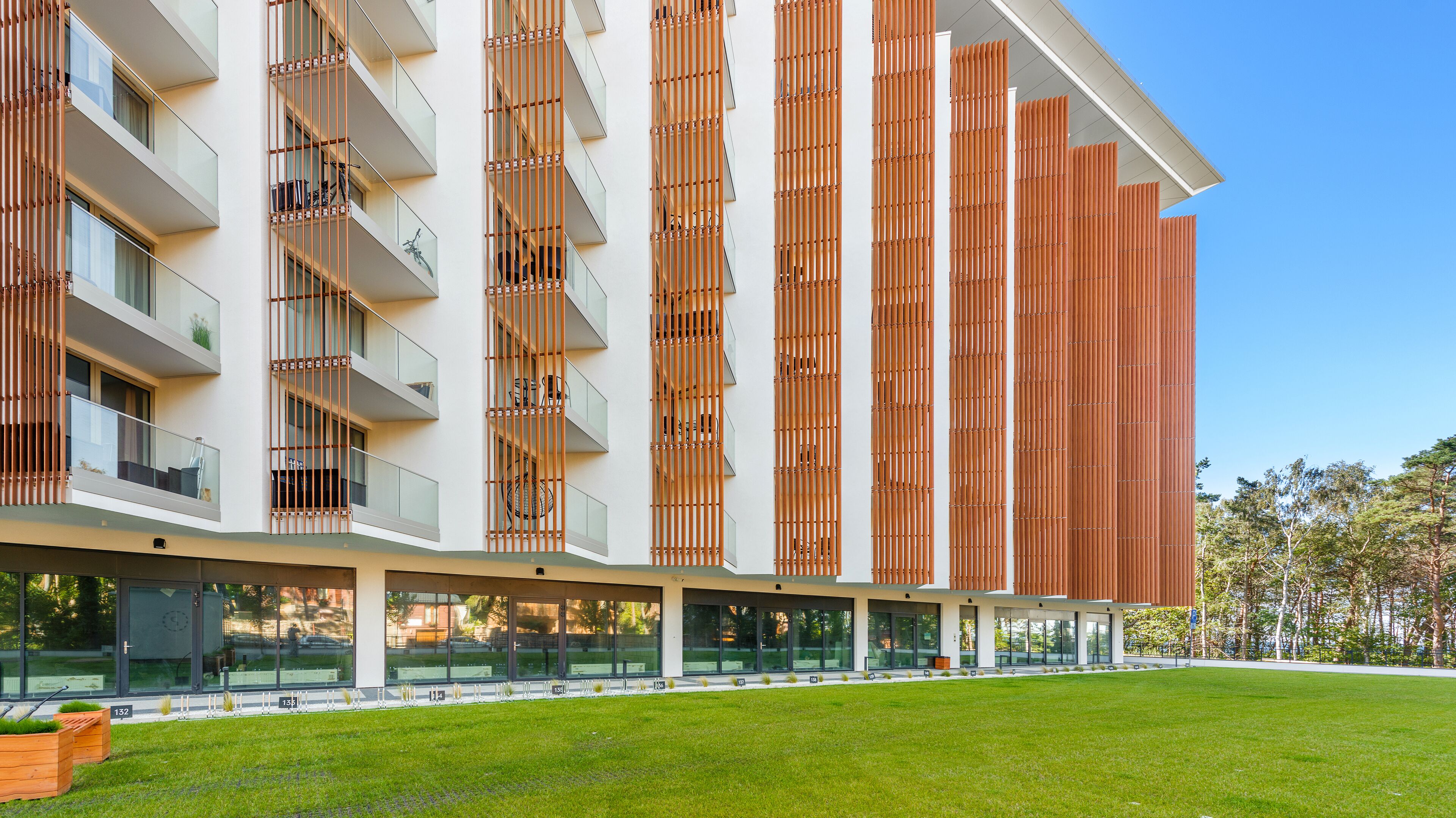 Un bâtiment moderne doté de nombreux balcons, de grandes fenêtres et d’une pelouse verdoyante à l’avant.