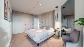 A modern bedroom with a large bed, a chair, a small table, and a mirror. - Apartamenty Sun & Snow Qinea (Rewal)