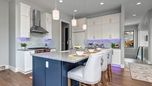 Una cocina moderna con una isla central, iluminación colgante y armarios blancos.