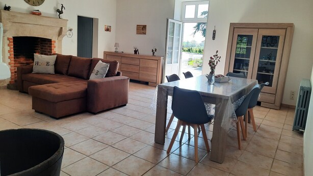 Un salon comprenant un canapé, une table à manger avec des chaises, une cheminée et une grande fenêtre.