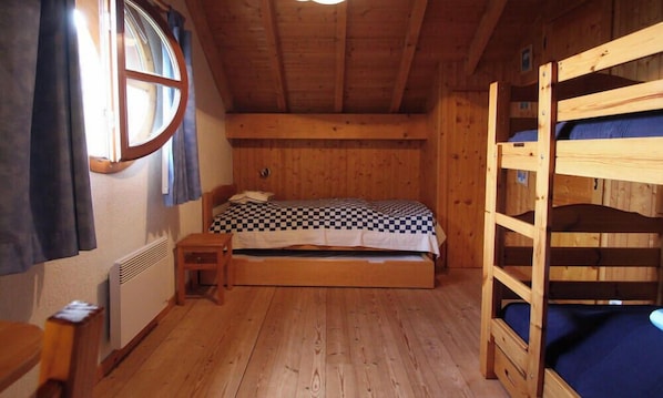 Una habitación de madera con una cama nido, una mesita de noche pequeña y una ventana con cortinas.