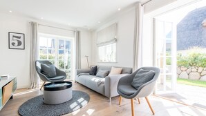 Una sala de estar moderna con un sofá gris, dos sillones, una mesita de centro y un amplio ventanal con vistas al exterior.