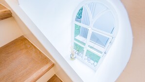 Una escalera de madera que sube hacia una pared blanca con una ventana.