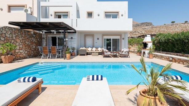 Una casa moderna con piscina, mobiliario exterior y un muro de piedra.