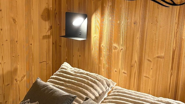 A wooden wall with a wall-mounted light fixture and a bed with two pillows. - 2-room cabin apartment for 4, south-facing terrace (Valloire)