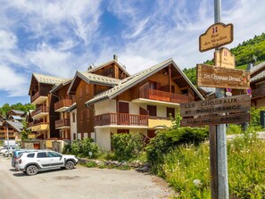 Un edificio de estilo chalet de madera con balcones, un letrero que dice 'Rue des Choseaux-Ville' y una señal de estacionamiento.