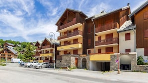 A multi-story hotel with balconies, a stone facade, and a parking area. - 2-room cabin apartment for 4, south-facing terrace (Valloire)