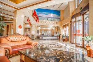 Vestíbulo de hotel con mostrador de recepción, un sofá de cuero, una mesa de centro de mármol y un piso grande con un motivo circular.