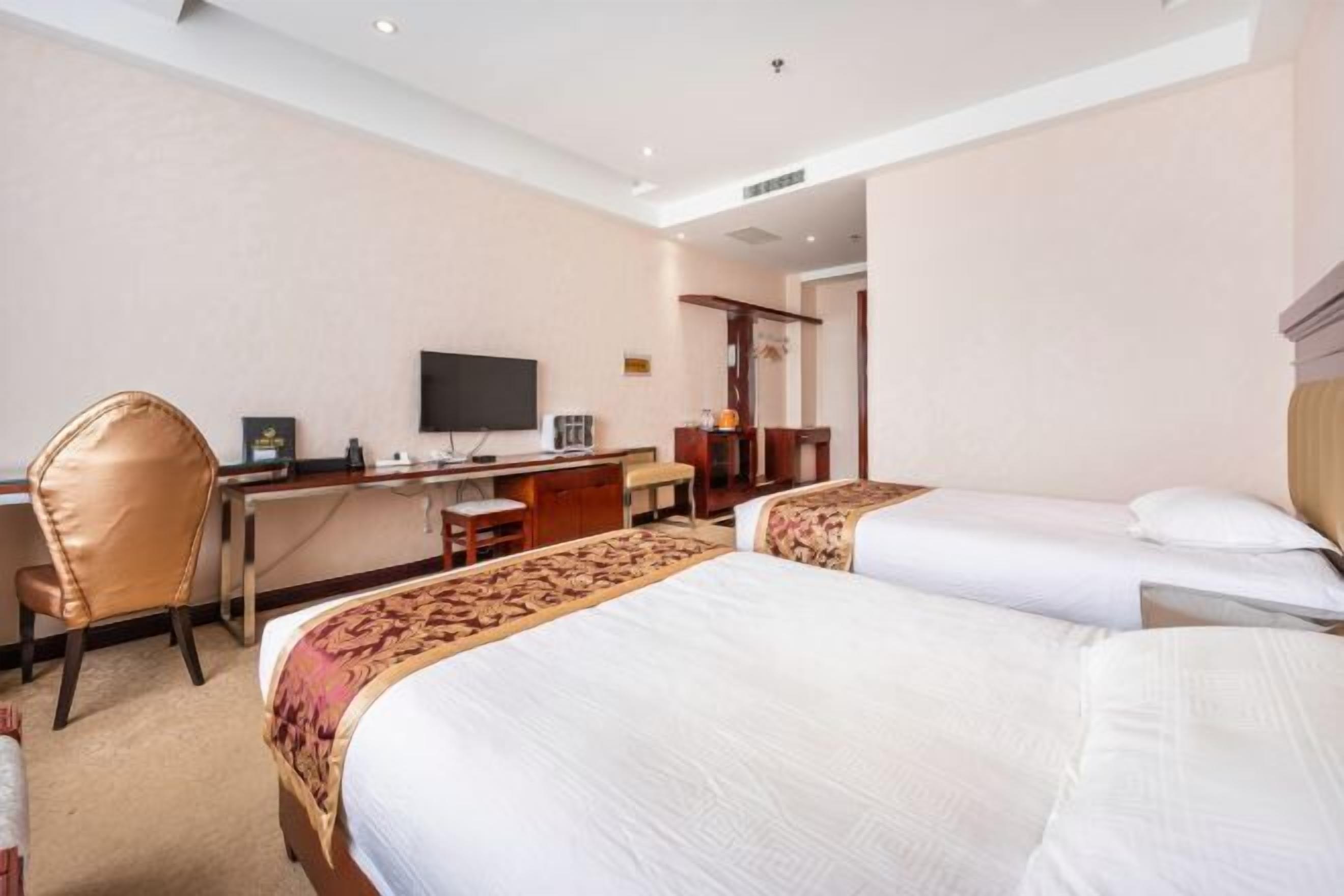 A hotel room with two beds, a desk, a chair, a television, and a door leading to another room.