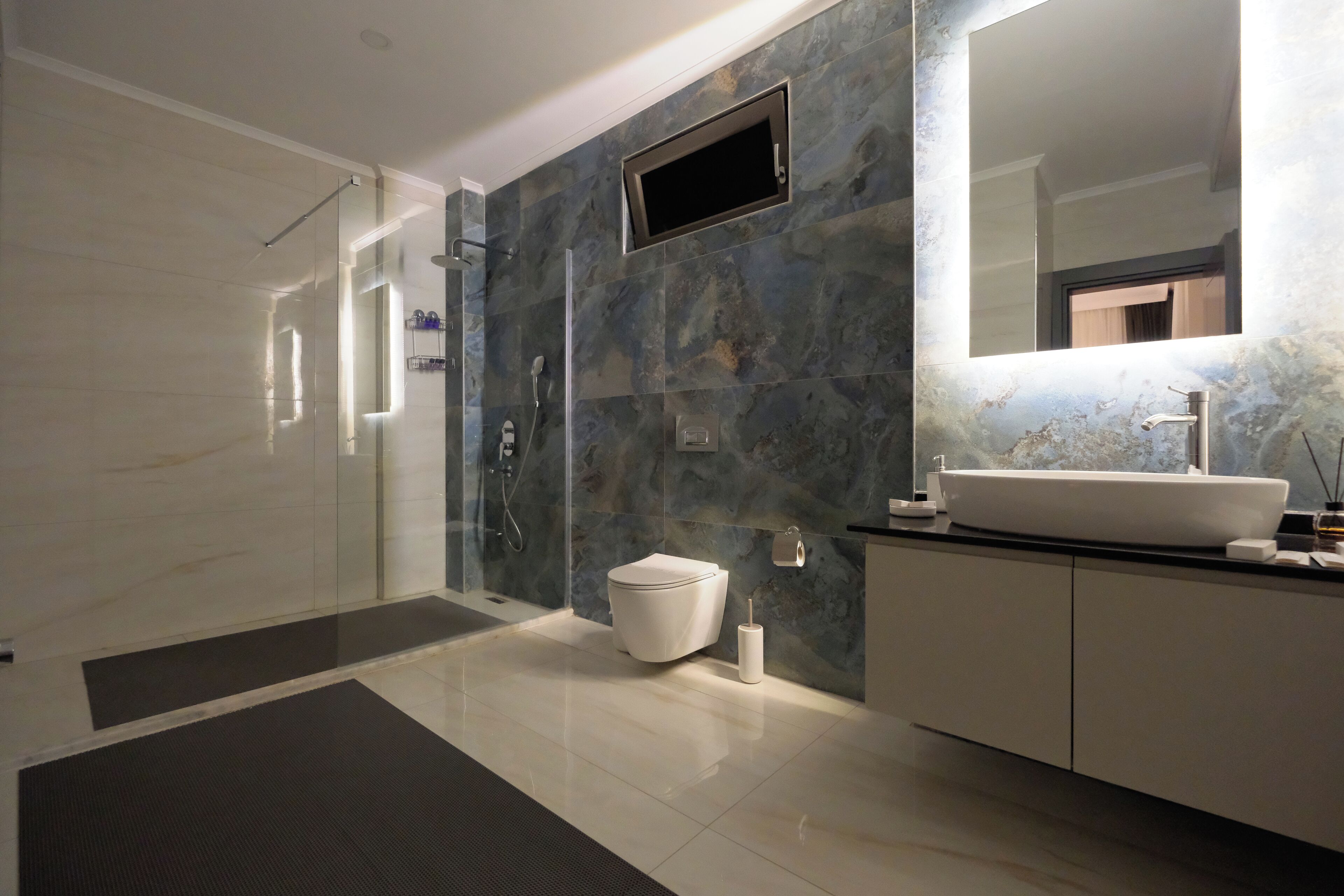 Een moderne badkamer met een douchecabine van glas, een wit toilet en een grote spiegel boven de wastafel.