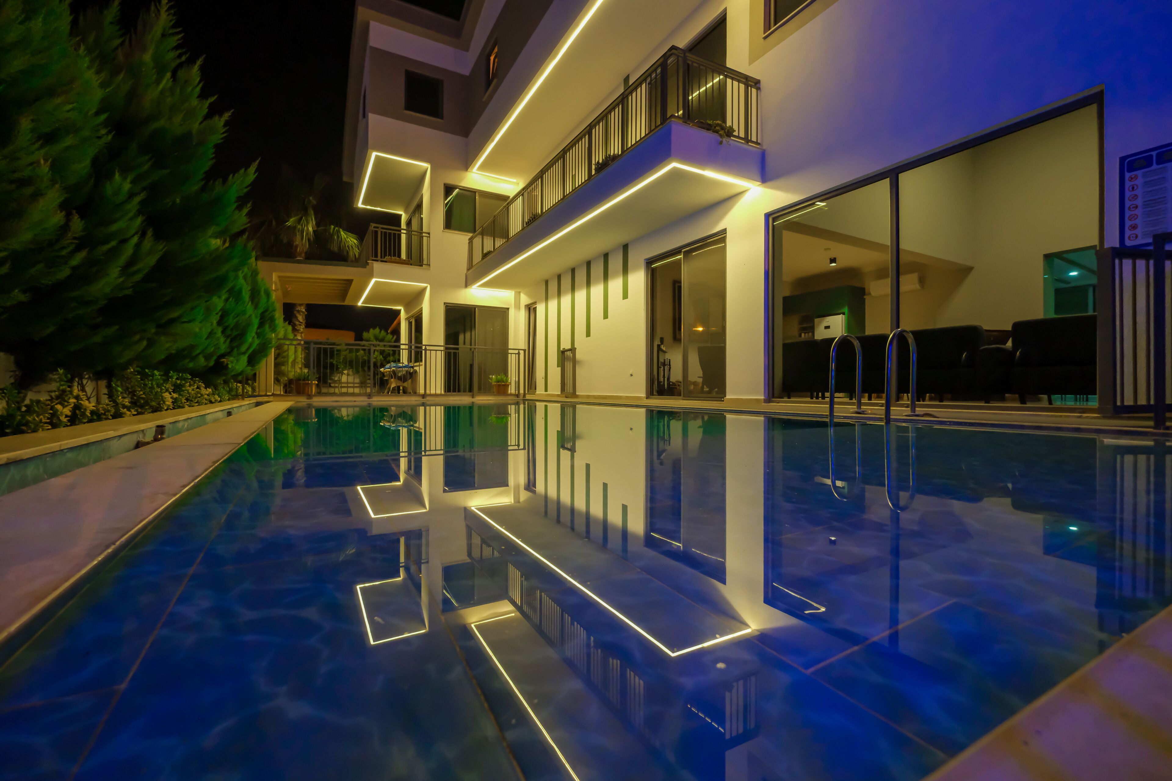 Un hotel moderno con piscina, mobiliario exterior y una zona de balcón bien iluminada.