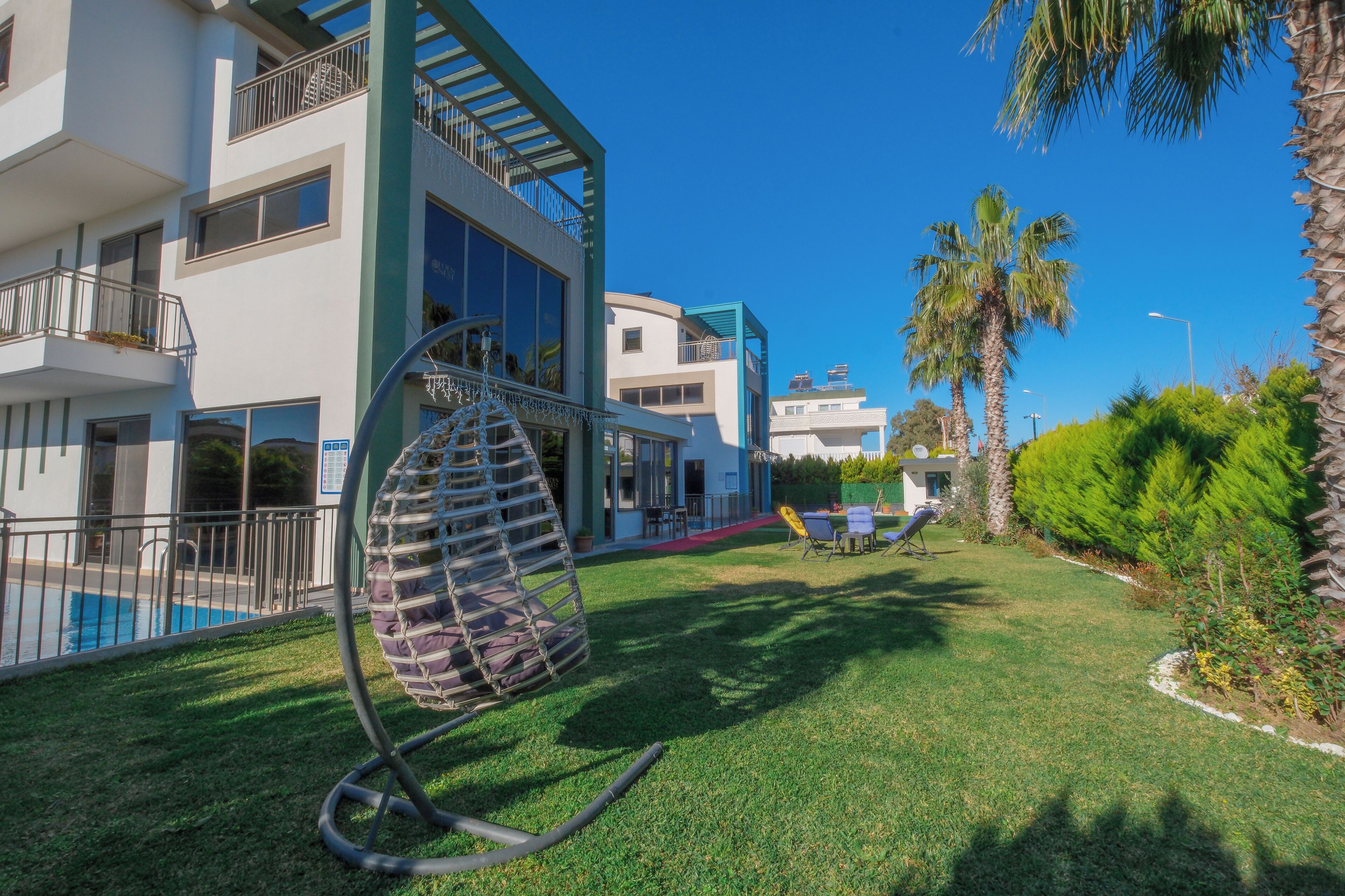 Un edificio moderno con piscina, zona de estar exterior y sillón colgante.