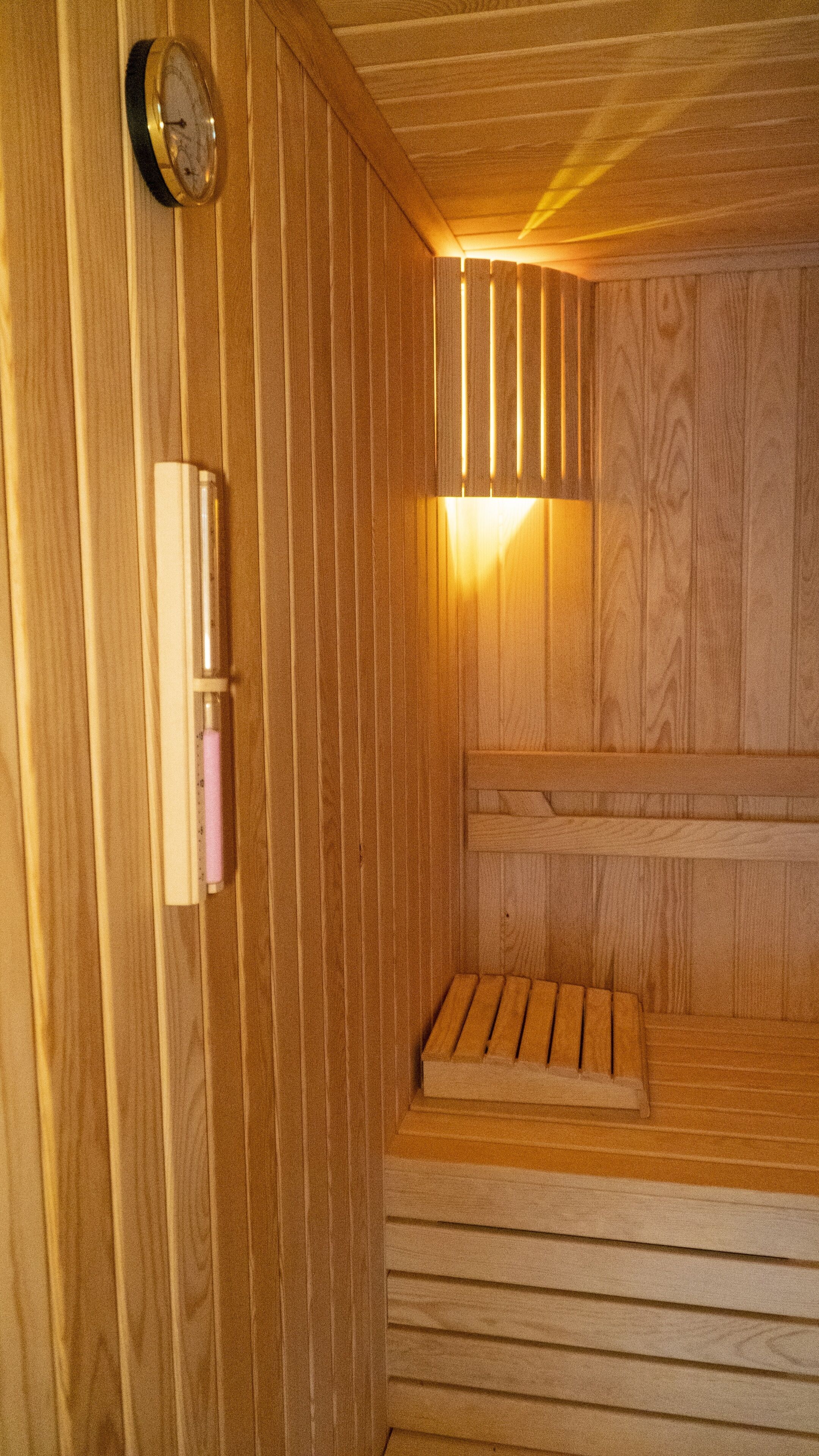 Een houten sauna met een bank, een klok aan de muur en een lamp.