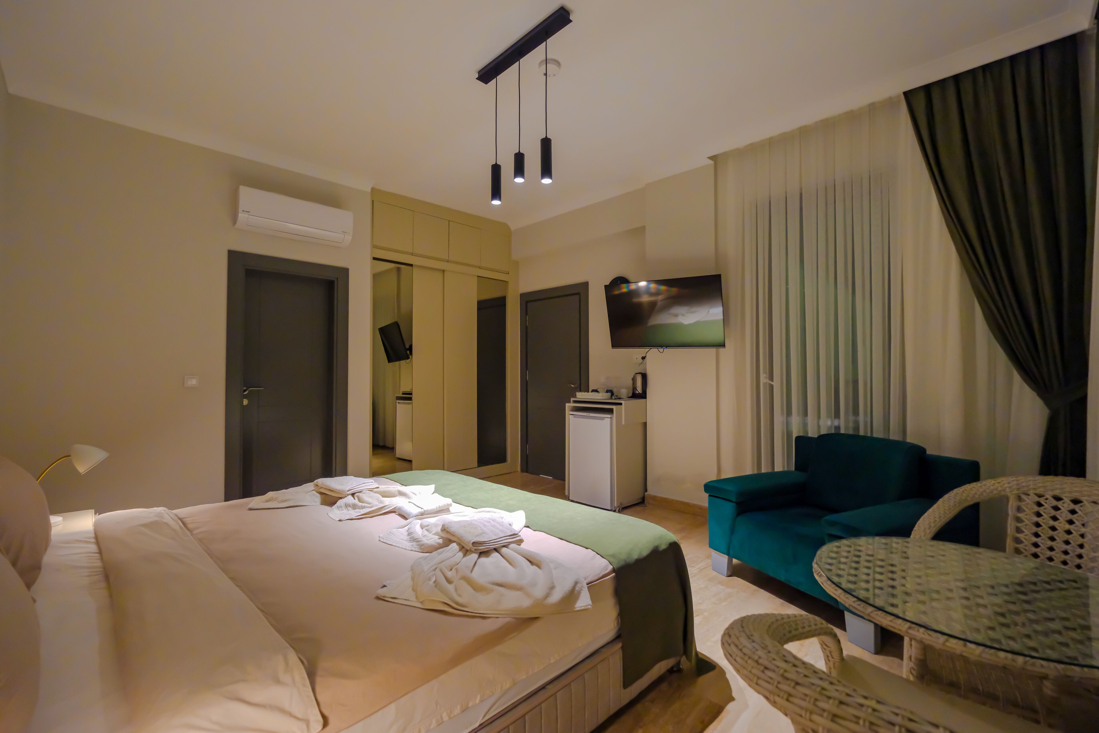 A hotel room with a bed, a sofa, a small table, a TV, and an air conditioning unit.